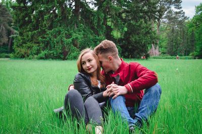 Portrait of couple sitting on grass against trees