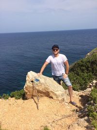 Portrait of young man standing on cliff against sea