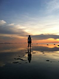 Rear view of silhouette woman standing on beach during sunset