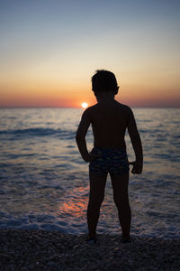 Rear view of man standing on beach during sunset