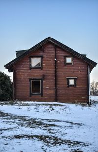 House on snow covered field against clear sky