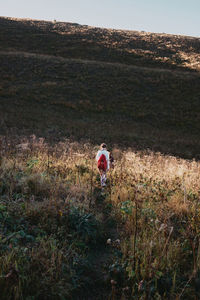 Rear view of woman wearing backpack on field against clear sky