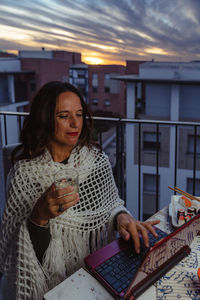 Pretty middle aged woman using laptop on outdoor balcony at sunset eating chinese food person