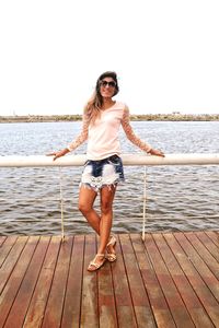 Portrait of young woman standing on pier over sea against clear sky