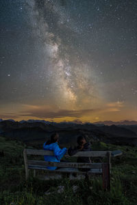 People sitting on bench at field against sky at night