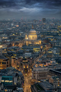 Aerial view of illuminated buildings against cloudy sky in city at dusk