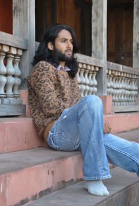 Side view of a attractive young guy with long hair, looking sideways while sitting in temple stairs
