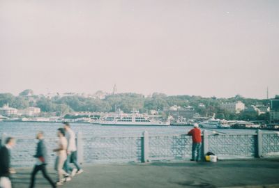 People by river in city against sky