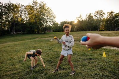 Smiling girl playing with balls while standing by male friend on grass in playground