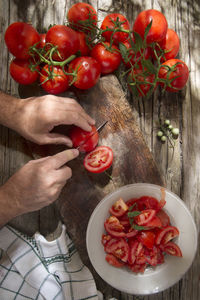 Cropped hands of man cutting cherry tomatoes on table