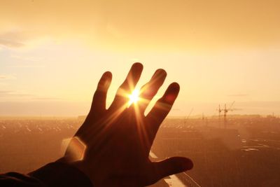 Cropped hand of man against sun during sunset