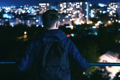 Rear view of man standing in front of illuminated lights at night