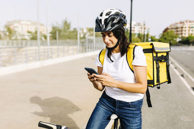 Female delivery person with bicycle using mobile phone on sunny day