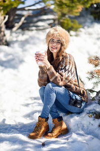 Portrait of smiling woman sitting on snow outdoors