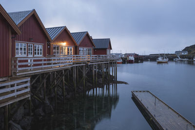 Wooden posts on lake by houses against sky