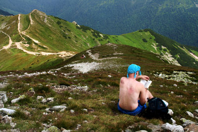 Midsection of man sitting on mountain against sky