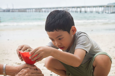 Cropped hands of granddaughter and son making sandcastle at beach