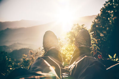 Low section of man relaxing on mountain against sky during sunset