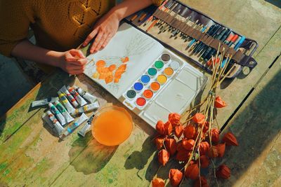 Cropped image of female artist painting flowers in notebook