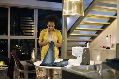 Female entrepreneur stitching jeans while standing by table in office