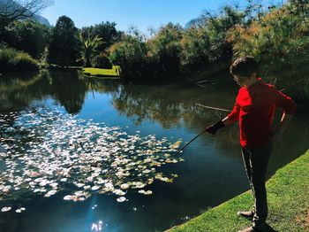 Full length of boy holding stick at lakeshore in park during sunny day