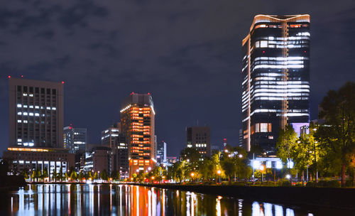 Illuminated buildings by river against sky at night