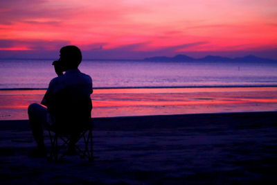 Rear view of silhouette man sitting on beach