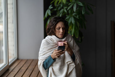 Sick woman holding smartphone letting boss know about illness while suffering from flu cold at home