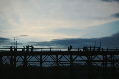 Silhouette people on bridge against cloudy sky