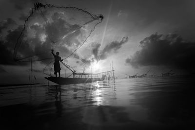 Silhouette fishing net on sea against sky