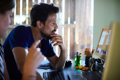 Male and female coworkers discussing at computer desk in creative office