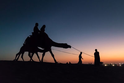 Silhouette people riding horse against sky during sunset