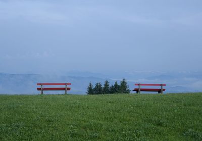 Empty bench on field against sky