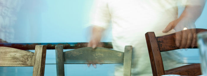 Midsection of man holding chairs against wall