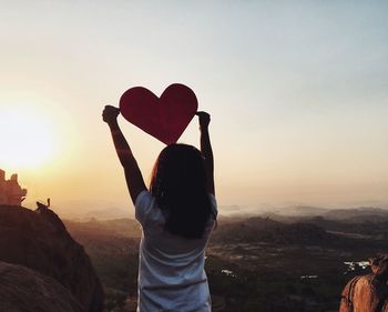 Rear view of woman holding heart shape paper against clear sky