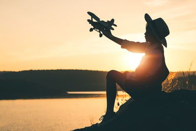 Silhouette woman by lake against sky during sunset