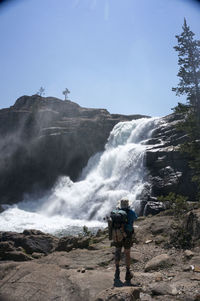 Rear view of man standing by waterfall against clear sky