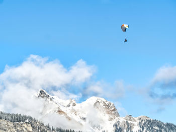 Person paragliding over snowcapped mountain against sky