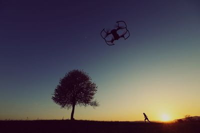 Silhouette person on field with drone against clear sky during sunset