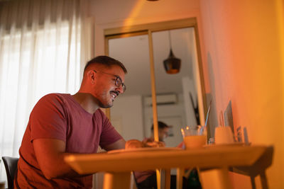 From below content male browsing on laptop while sitting at table with tablet and desserts in hotel room