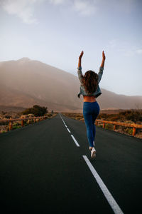 Rear view of woman jumping on road against mountain