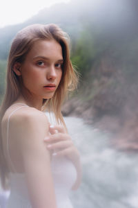 Portrait of beautiful young woman standing by river