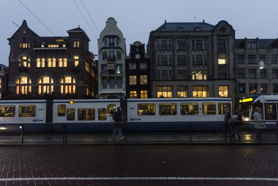 Illuminated buildings by street against sky at dusk