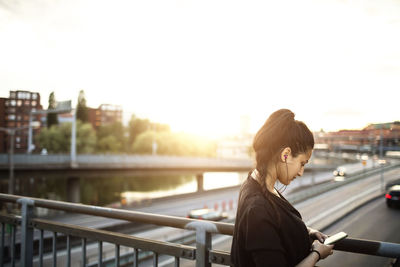 Side view of woman using mobile phone while on standing bridge against sky