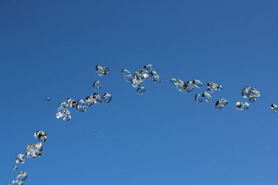 Low angle view of bubbles against clear blue sky