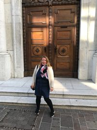 Portrait of woman standing against door of building