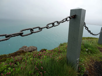 Barbed wire fence by sea against sky