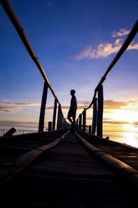 Surface level shot of man standing on jetty over sea at sunset