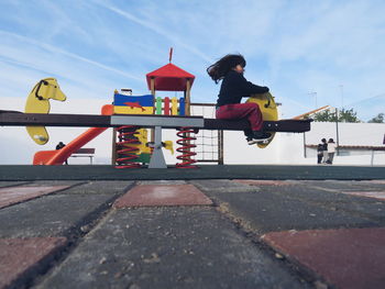 Side view of girl sitting on play equipment