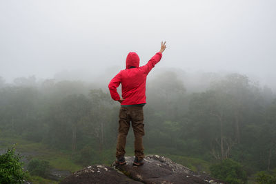 Rear view of man gesturing while standing on rock against sky